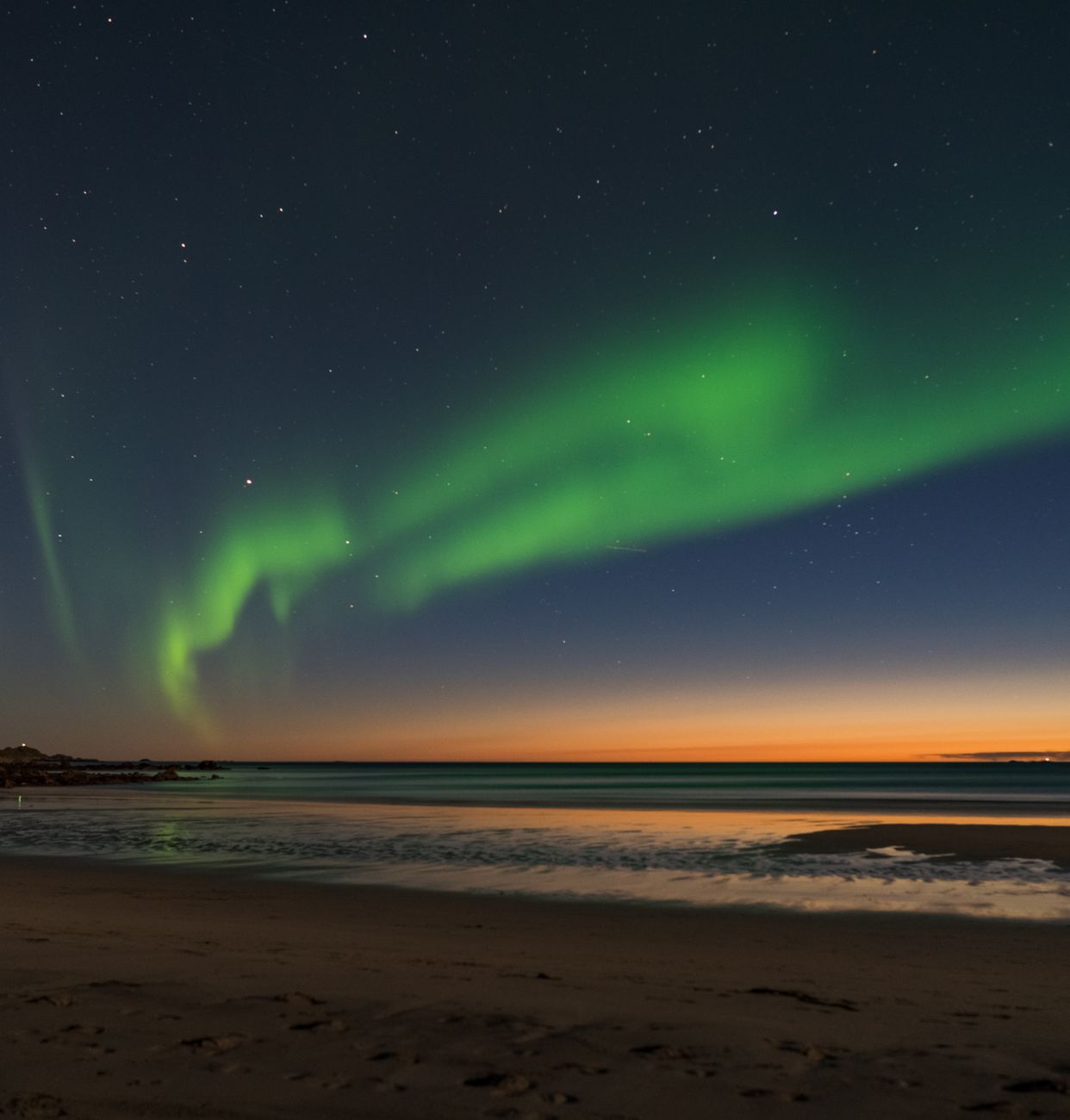 Stunning view of the aurora borealis dancing over a tranquil beach in Nordland, Norway at twilight.